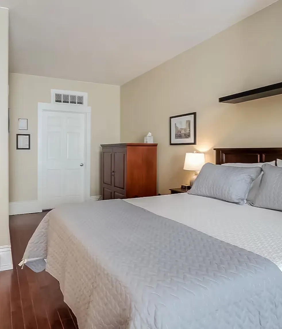 Quiet guest suite bedroom with warm lighting, neutral tones, and wooden headboard and chest