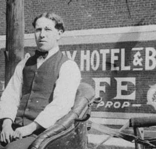 Black-and-white portrait of man in waistcoat with hotel bar sign backdrop