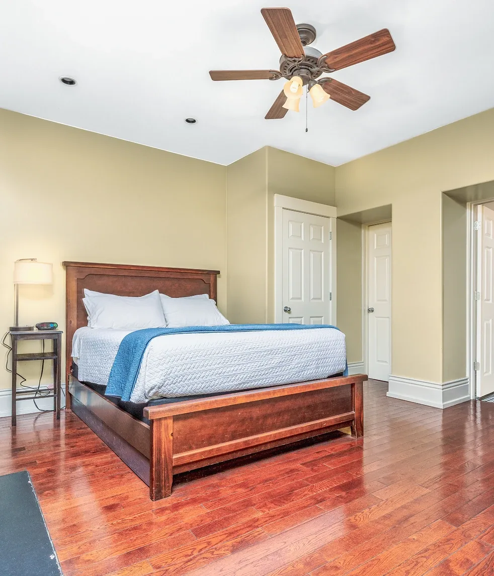 Inviting neutral guest bedroom with modern dark wood bed, white linens, ceiling fan, and warm hardwood floors