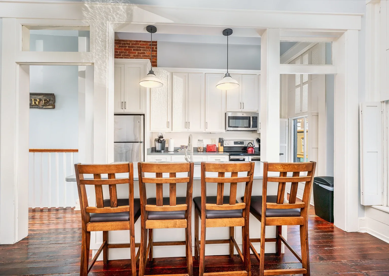 Open-plan white kitchen with wood bar chairs and pendant lights over the island
