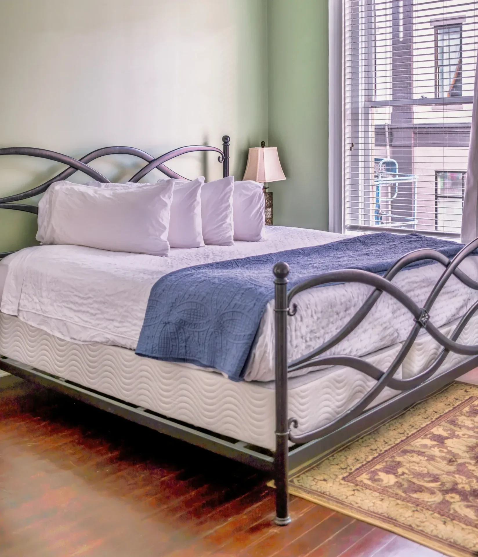 Modern downtown bedroom with dark metal bed frame, white linens, blue throw, and daylight blinds