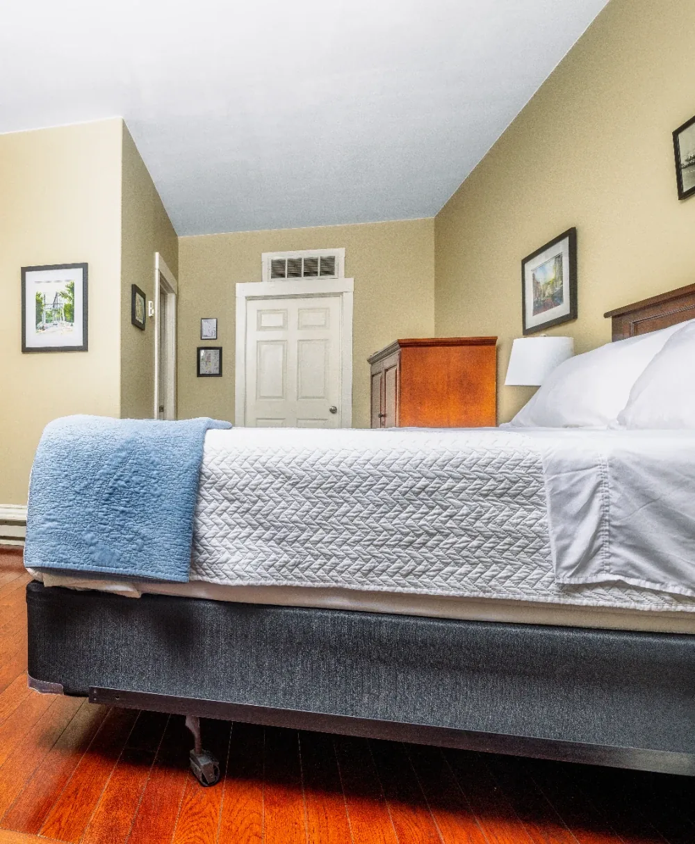 Minimalist guest bedroom from bed foot perspective with tidy linens, warm wood floor, and dresser