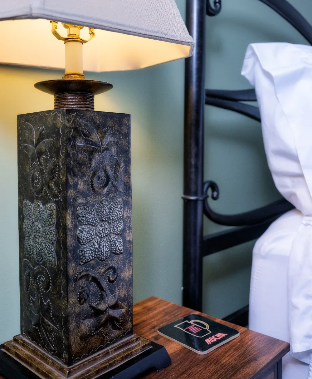 Cozy bedside lamp with warm glow, rustic carved base, and black metal headboard in a tidy room.