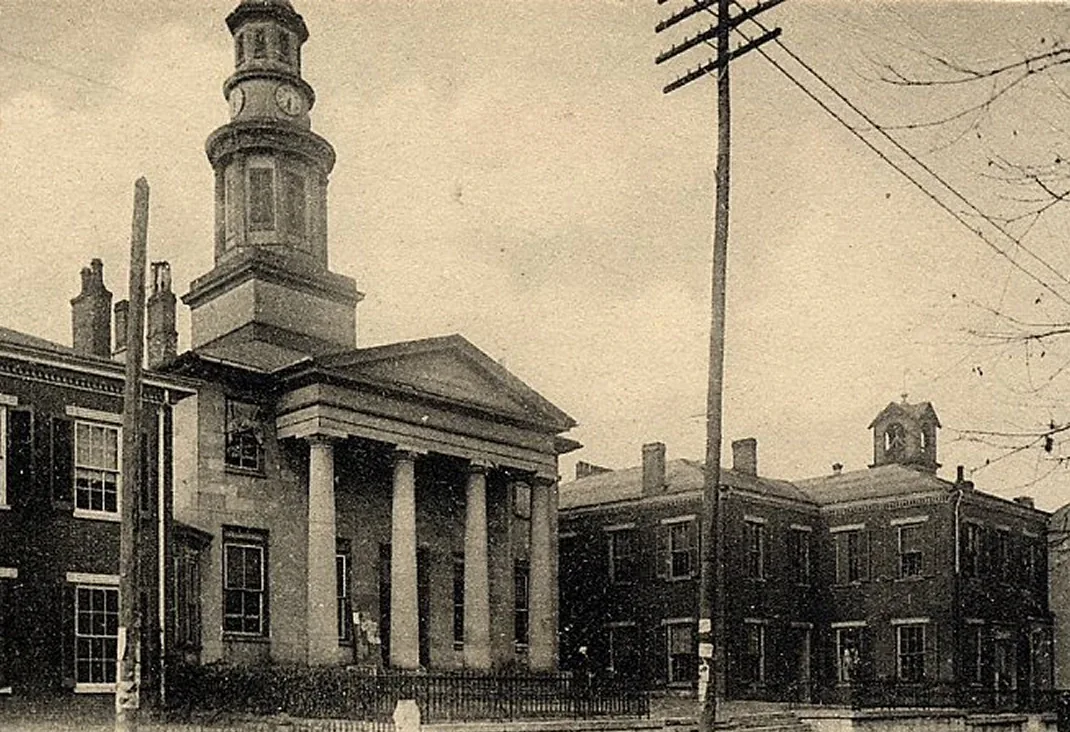 Classical brick building with portico columns, tower cupola, and civic windows along a street
