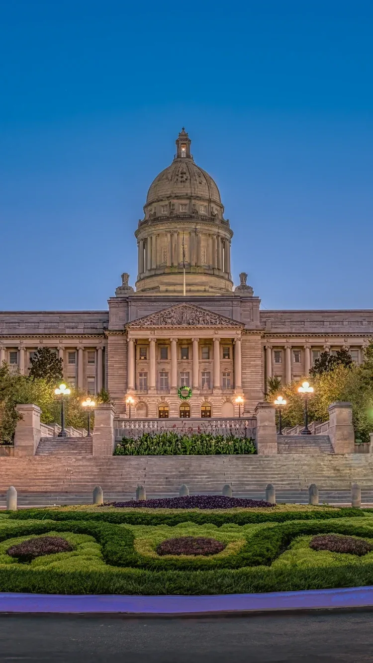 Grand illuminated civic dome at dusk, formal steps, classic columns, and symmetrical gardens