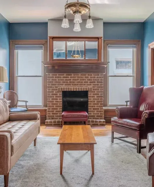 Cozy blue living room with brick fireplace, nautical print, and symmetrical mid-century seating