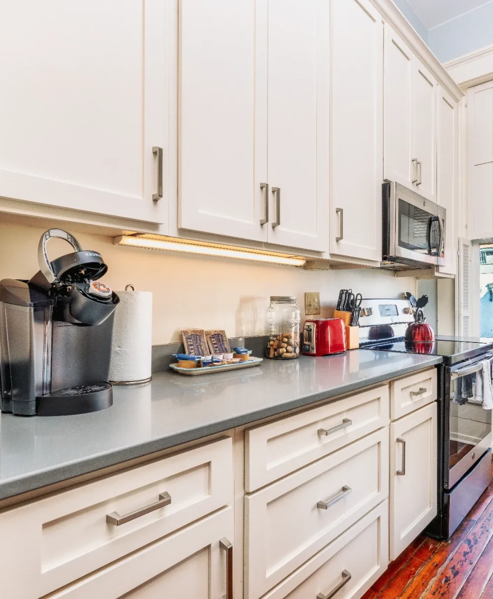 Bright white shaker galley kitchen with stainless oven, gray counters, and warm wood floors