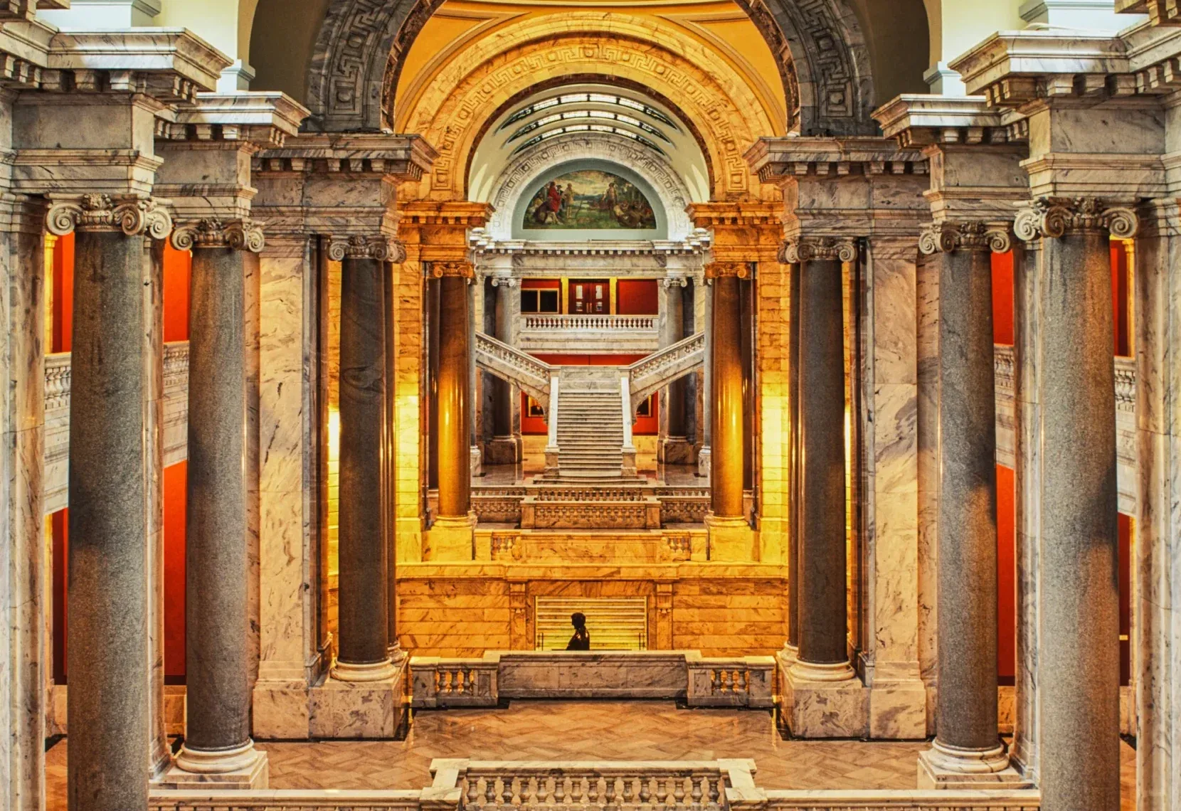 Grand ceremonial colonnade interior with fluted columns, arches, steps, and a bright central opening.