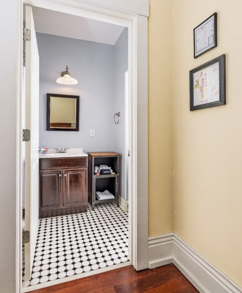 Charming hallway view into gray bathroom with dark vanity, patterned tile floor, and towel storage