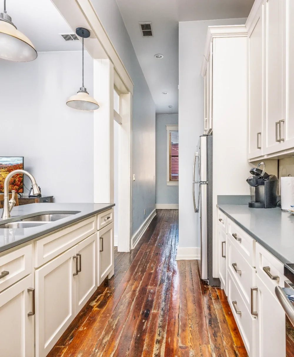 Bright white galley kitchen with wood floors, gray countertops, and stainless refrigerator.