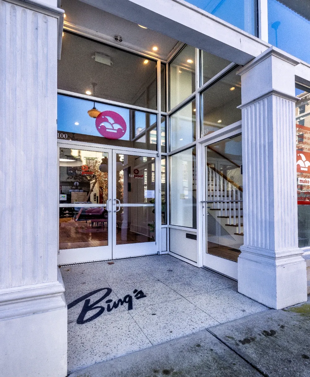 Modern bistro entrance with glass doors, fluted columns, and warm interior staircase in arcade
