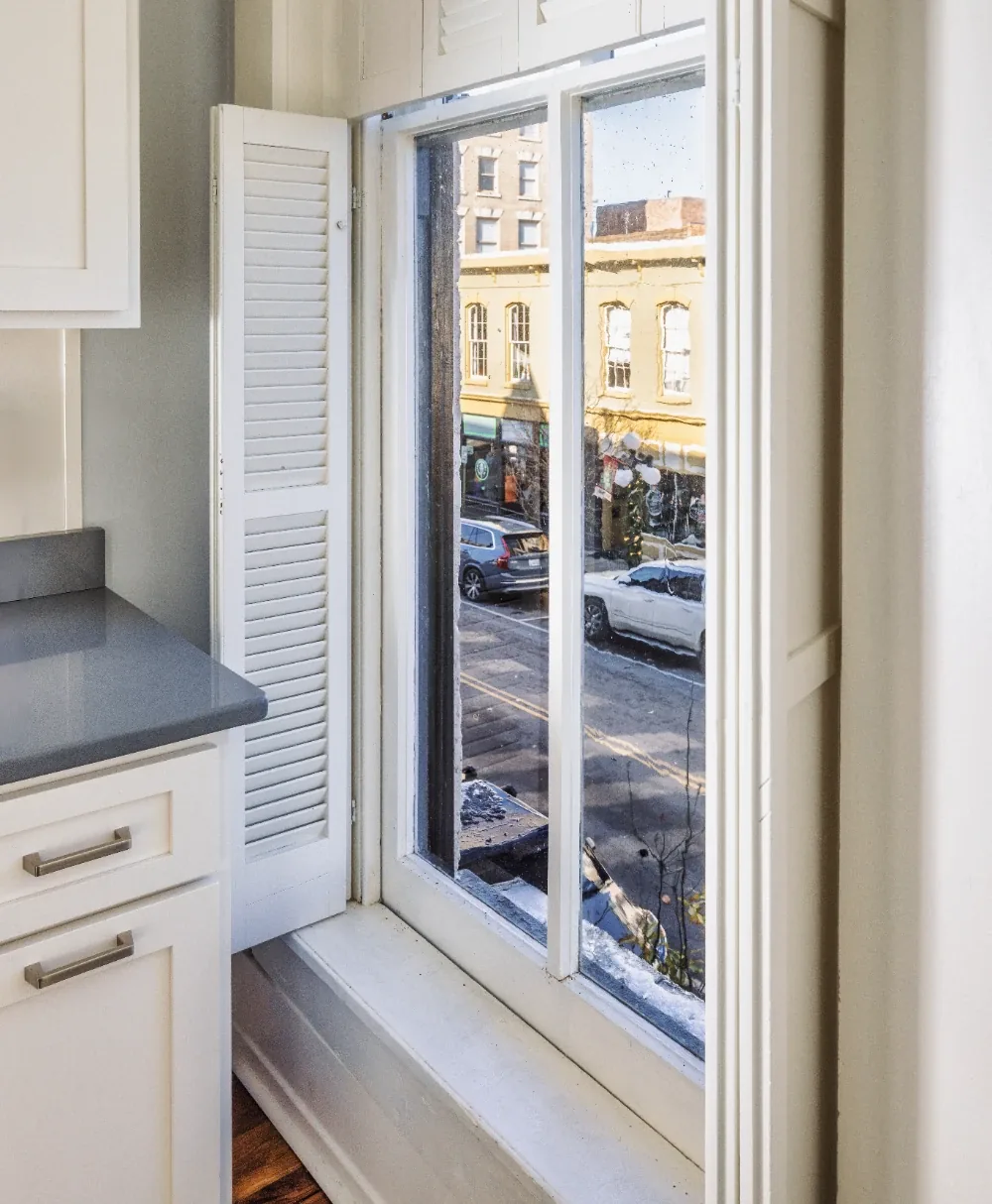 Modern kitchen nook with window shutters, gray countertops, and urban street view