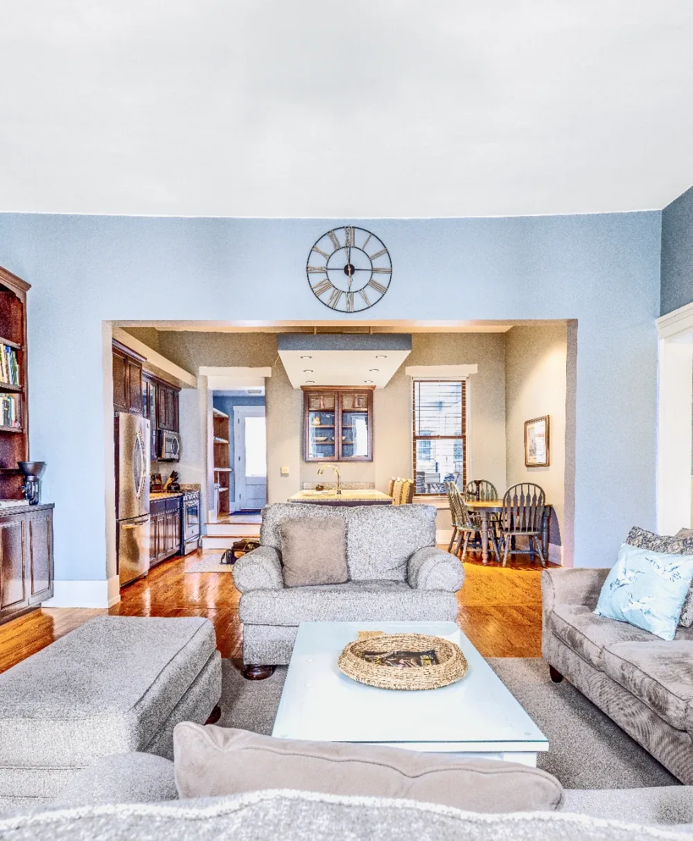 Open blue living and dining room with neutral sofa seating, hardwood floors, and coffee tray