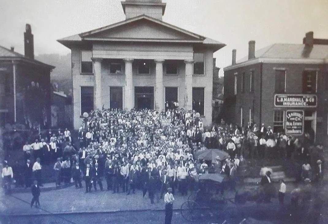 Historic downtown crowd fills courthouse steps with early cars, black-and-white civic scene