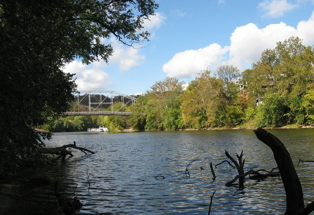 Sunny river reflections with bridge in distance, blue sky and autumn treeline scenery