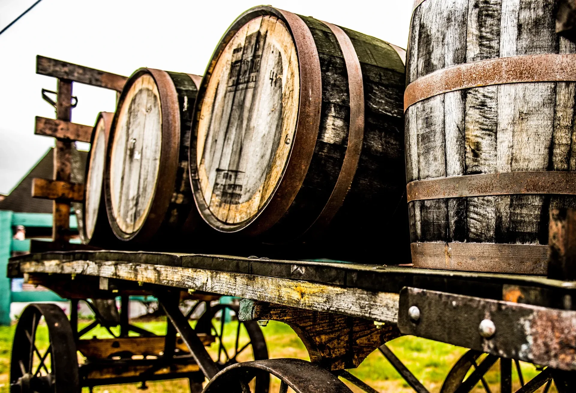 Rustic wooden wagon loaded with textured oak barrels, weathered staves, rusted hoops, rural outdoor still life
