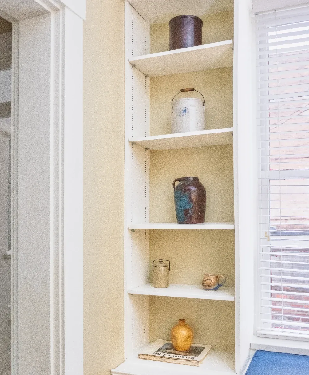Sparse built-in shelving niche with warm neutral decor, minimal pottery and curated objects.