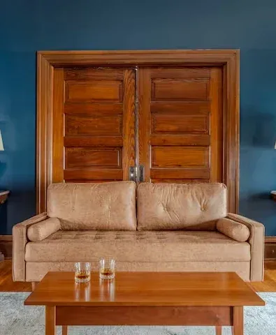 Symmetrical teal wall living room with warm wood double doors, tan sofa, and coffee glasses