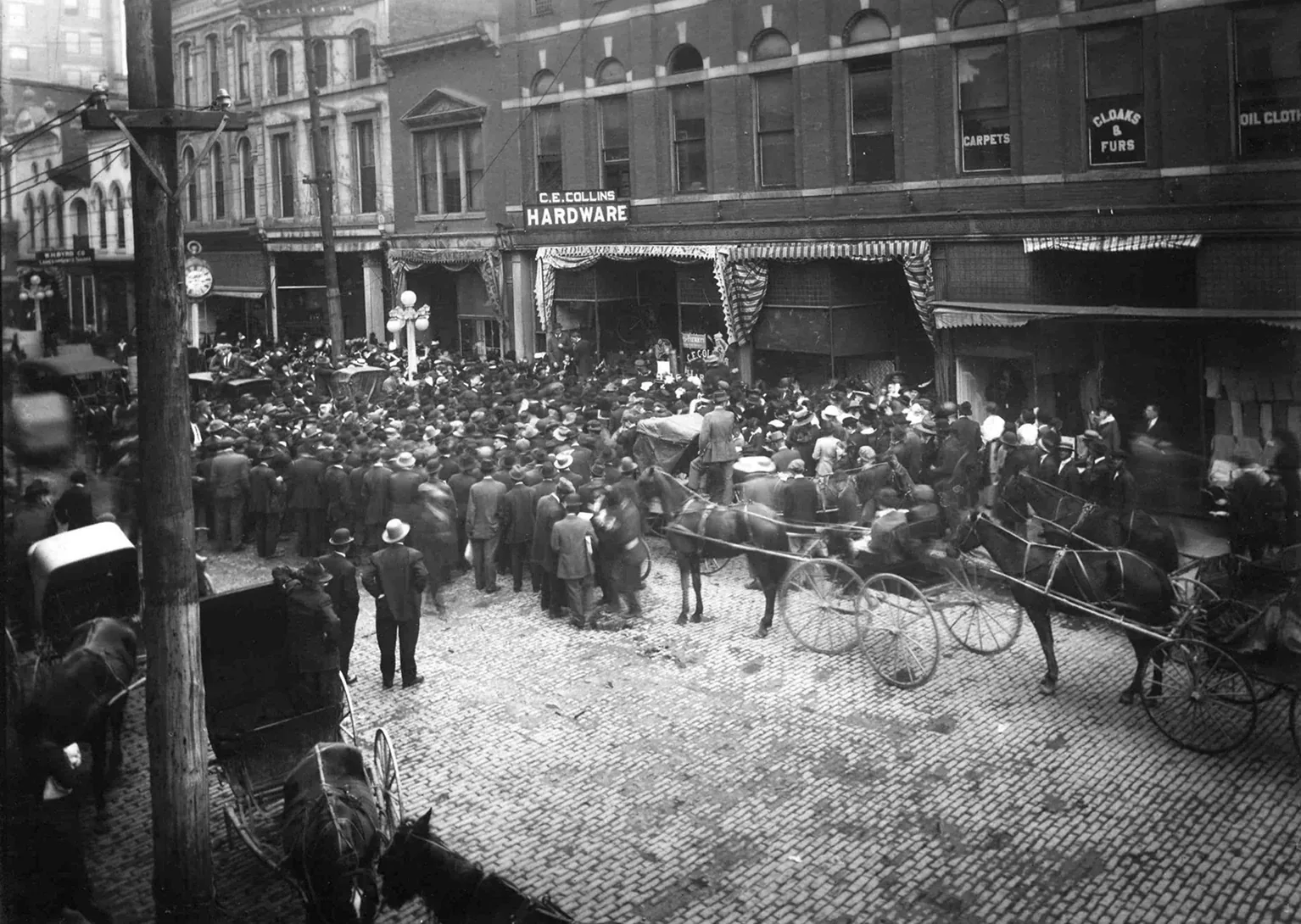 Historic Black-and-White Cobblestone Street Crowd Outside Shops With Horse-Drawn Wagons