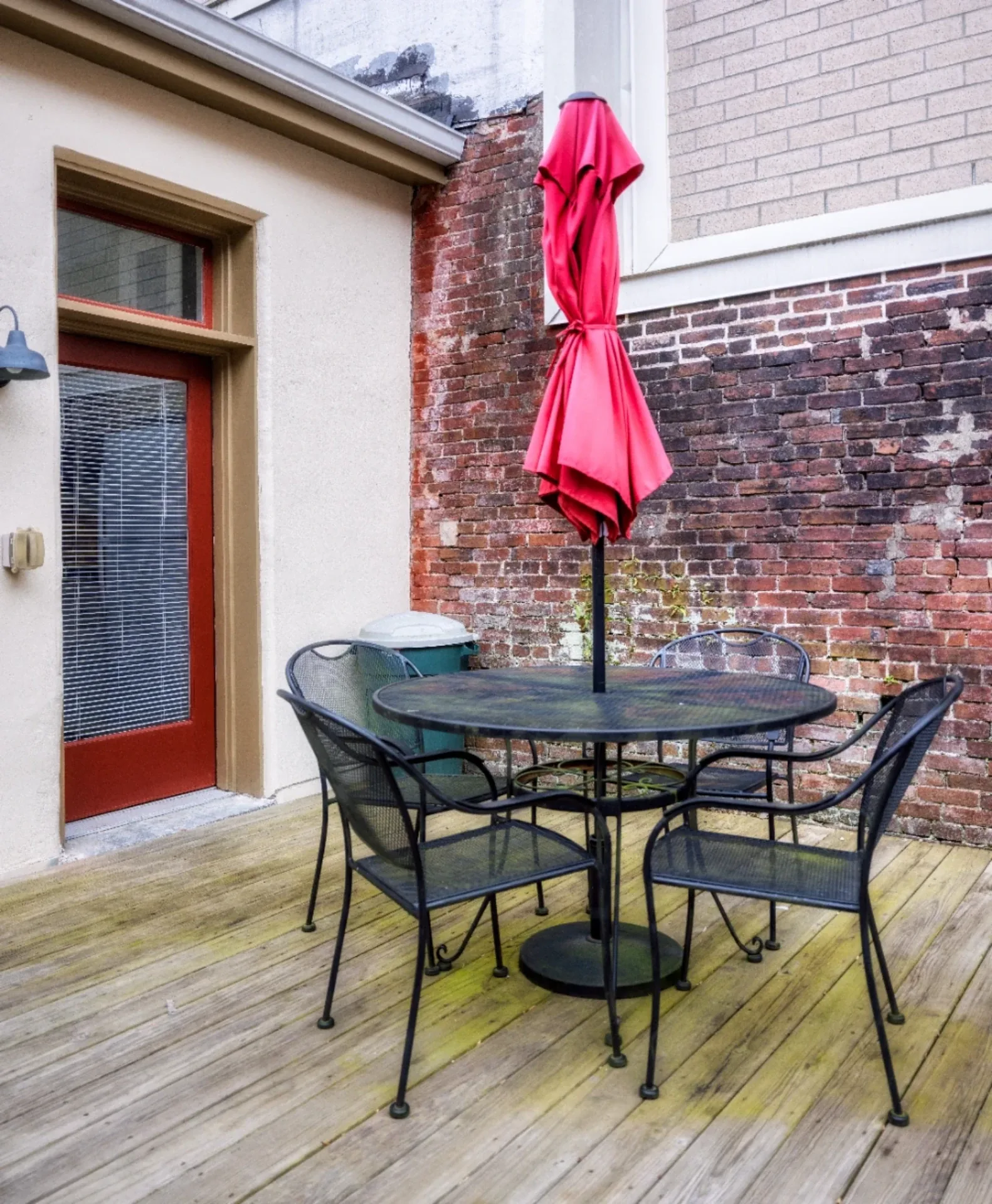 Urban brick and stucco patio with red umbrella, glass table, and metal chairs