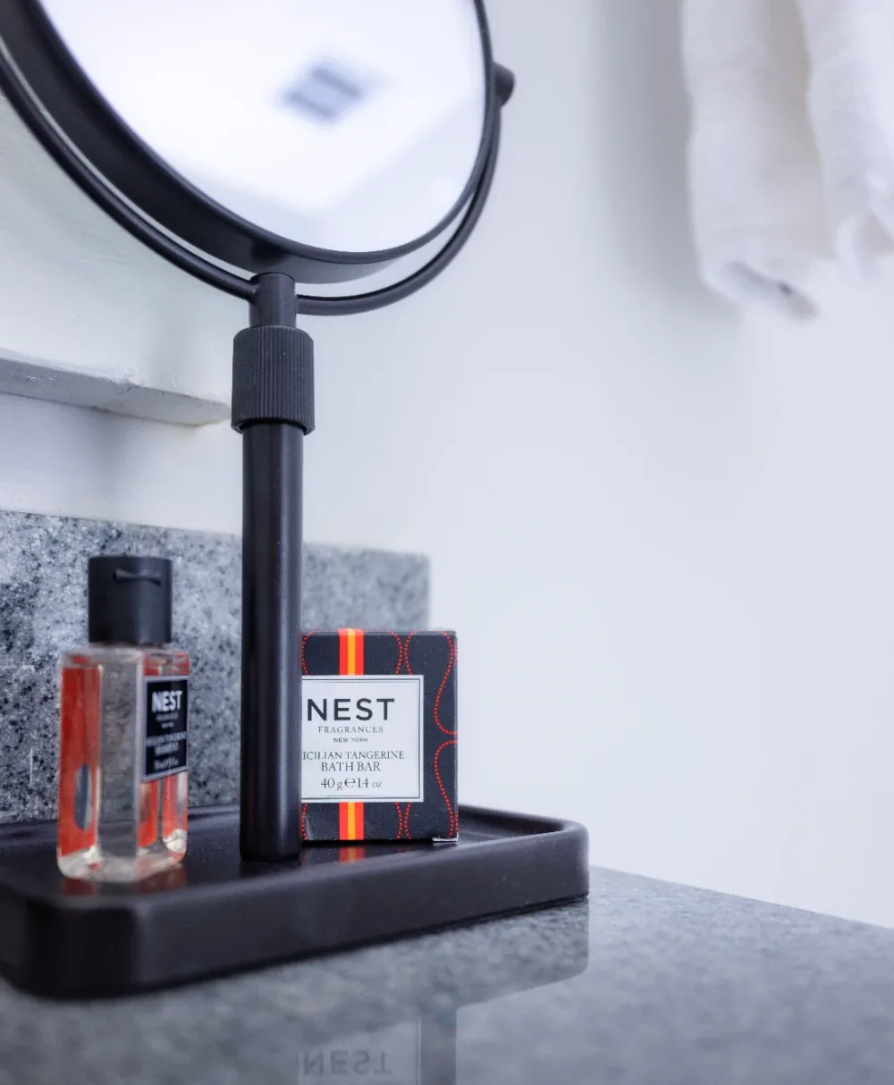 Matte black vanity tray with amber bottle, NEST box, and round makeup mirror.
