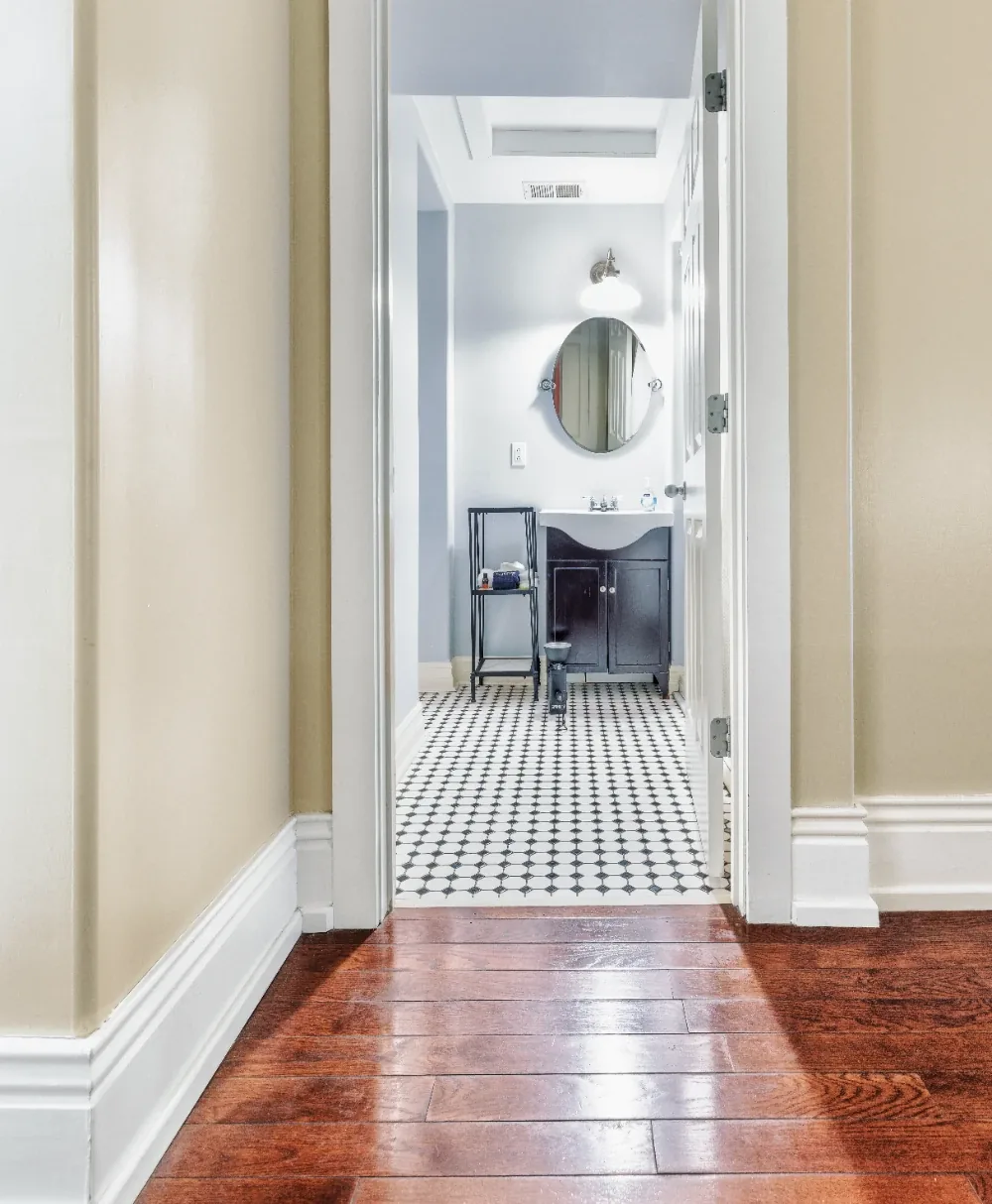 Warm hallway view with black-and-white tile bathroom, round mirror, and white trim doorway